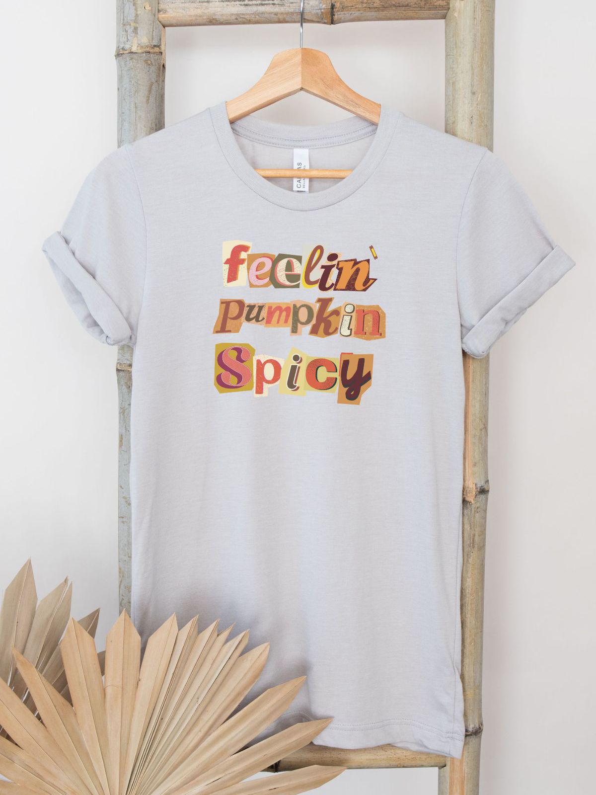 Feelin Pumpkin Spicy graphic t-shirt hanging on bamboo rack