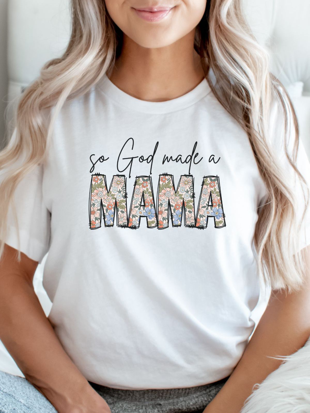 woman wearing a white t-shirt with floral text saying Mama
