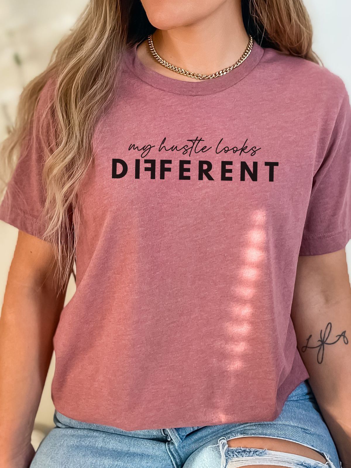 woman wearing a mauve t-shirt with text 'my hustle looks different'