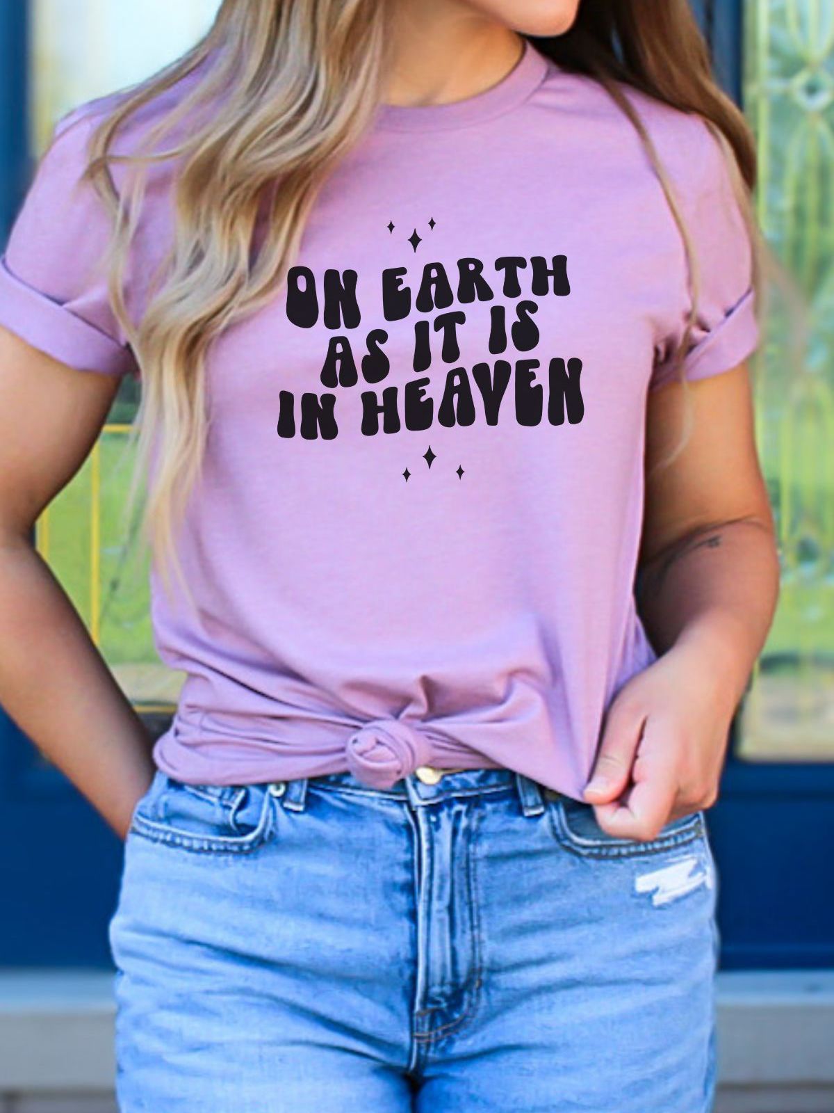 Woman wearing pink shirt with On Earth As It Is In Heaven text