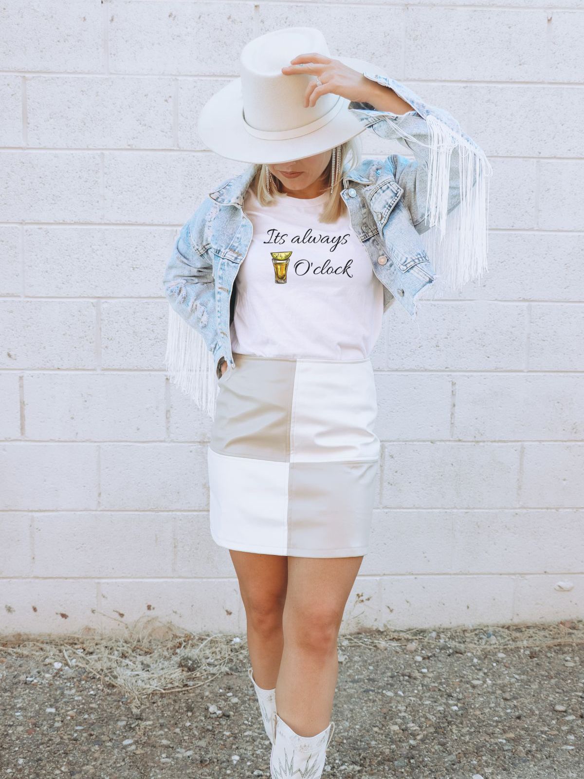 Woman wearing Its Always Oclock t-shirt with fringe jacket and hat