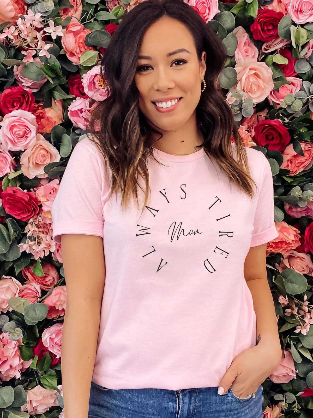 Woman wearing pink 'Always Tired Mom' t-shirt in floral background
