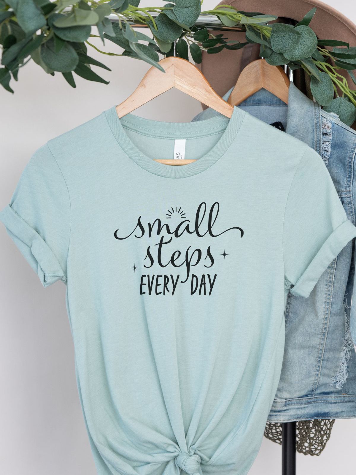 Small Steps Every Day motivational t-shirt on hanger with green leaves