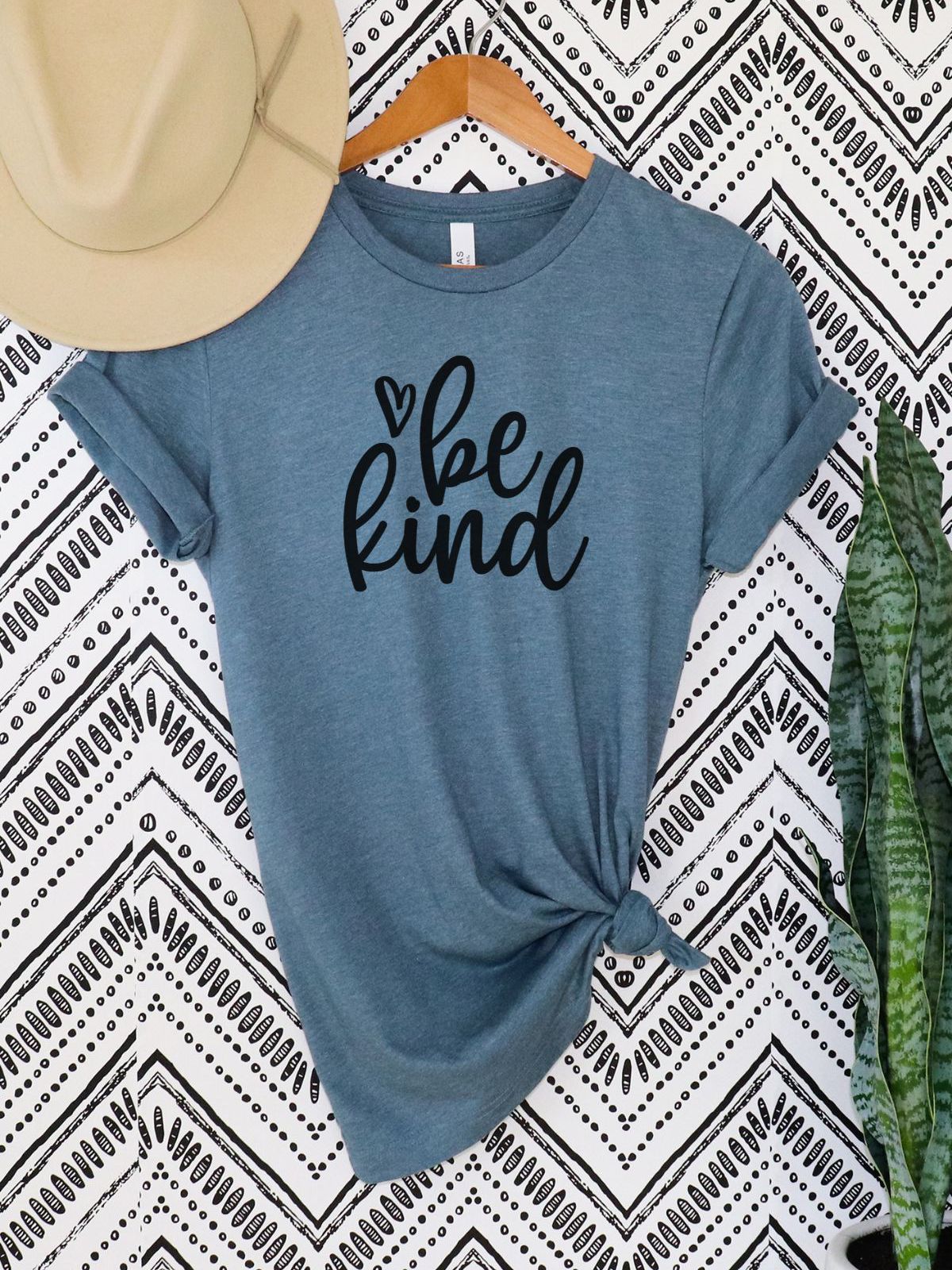 Be Kind T-Shirt hanging on hanger with pattern background