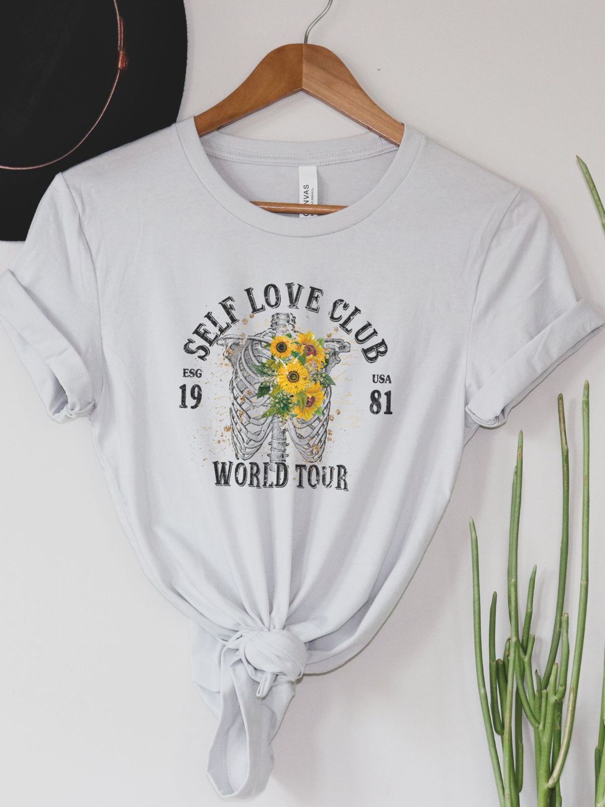 Self Love Club women's t-shirt with floral skeleton design on hanger
